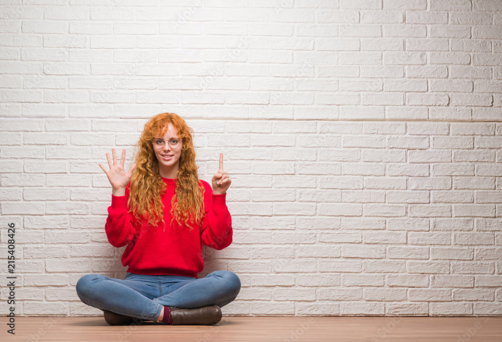 Young redhead woman sitting over brick wall showing and pointing up with fingers number six while smiling confident and happy. Young redhead woman sitting over brick wall showing and pointing up with fingers number six while smiling confident and happy.