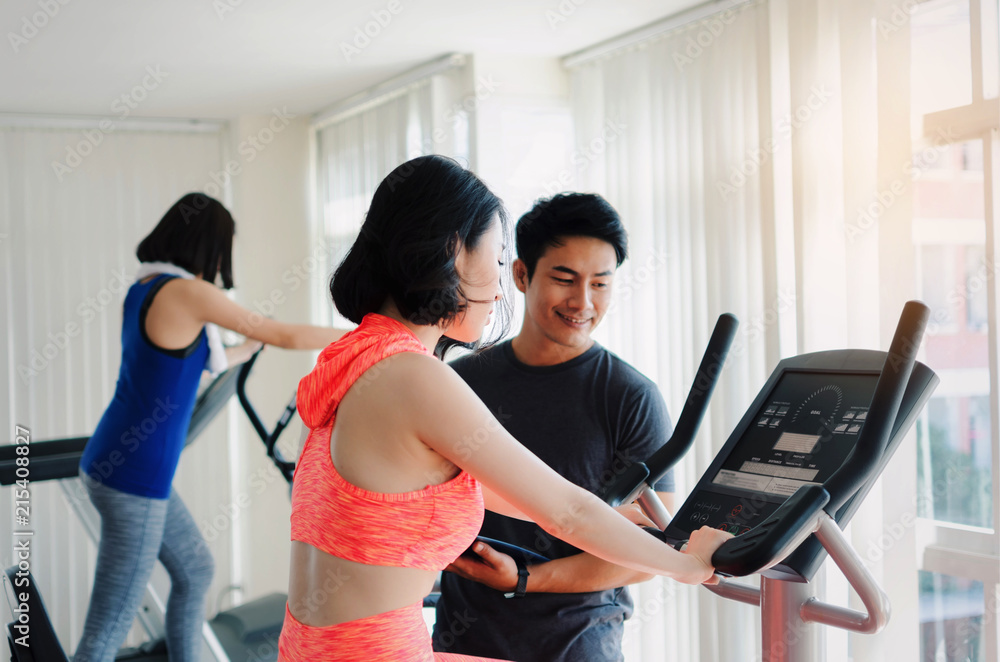 asian young woman slim body exercising on bicycle machine with young man personal trainer in fitness gym, bodybuilder, healthy lifestyle, fitness, workout and sport training concept asian young woman slim body exercising on bicycle machine with young man personal trainer in fitness gym, bodybuilder, healthy lifestyle, fitness, workout and sport training concept
