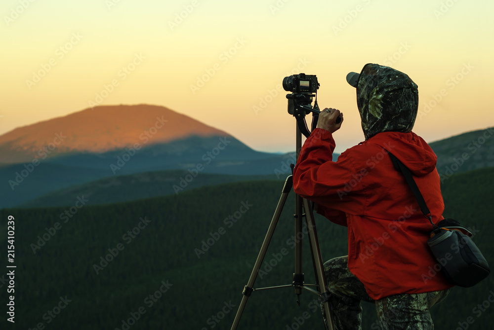 woman photographer takes a picture of a dawn in the mountains by camera on a tripod