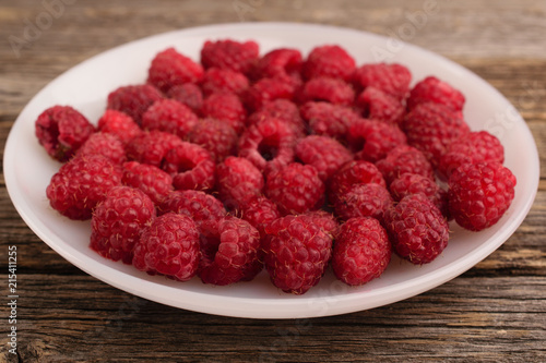 A plate full of raspberry on a wooden background