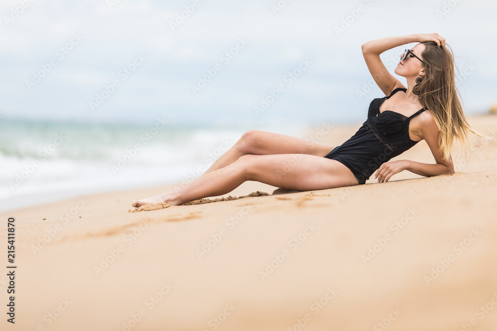 Beautiful young woman with perfect body lying down on the beach, tanning on a beach resort, enjoying summer vacation Beautiful young woman with perfect body lying down on the beach, tanning on a beach resort, enjoying summer vacation