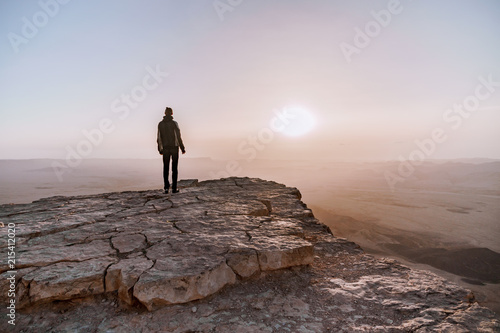 Alone man in israel negev desert admires the view of sunrise. Young male person stands on the edge of the cliff photo