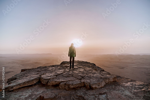 Alone man in israel negev desert admires the view of sunrise. Young male person stands on the edge of the cliff photo