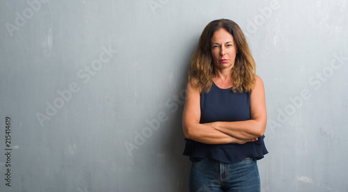 Middle age hispanic woman standing over grey grunge wall skeptic and nervous, disapproving expression on face with crossed arms. Negative person. © Krakenimages.com
