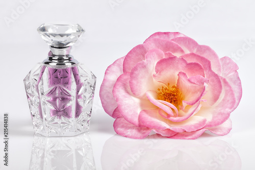 A bottle of rose cologne next to a rose on white background