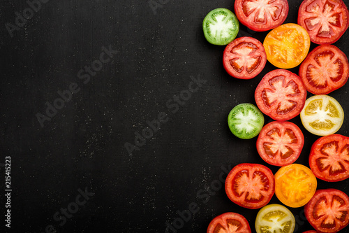 Red tomatoes of different colors cut in half. Juicy vegetables on black background, top view