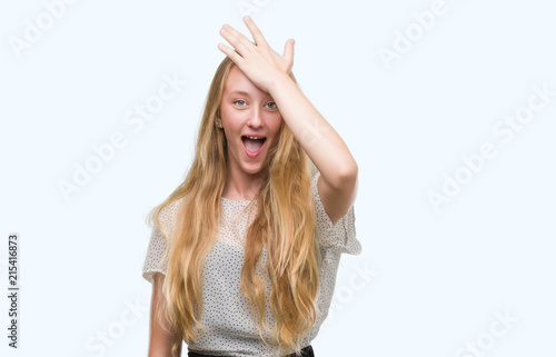 Blonde teenager woman wearing moles shirt surprised with hand on head for mistake, remember error. Forgot, bad memory concept.