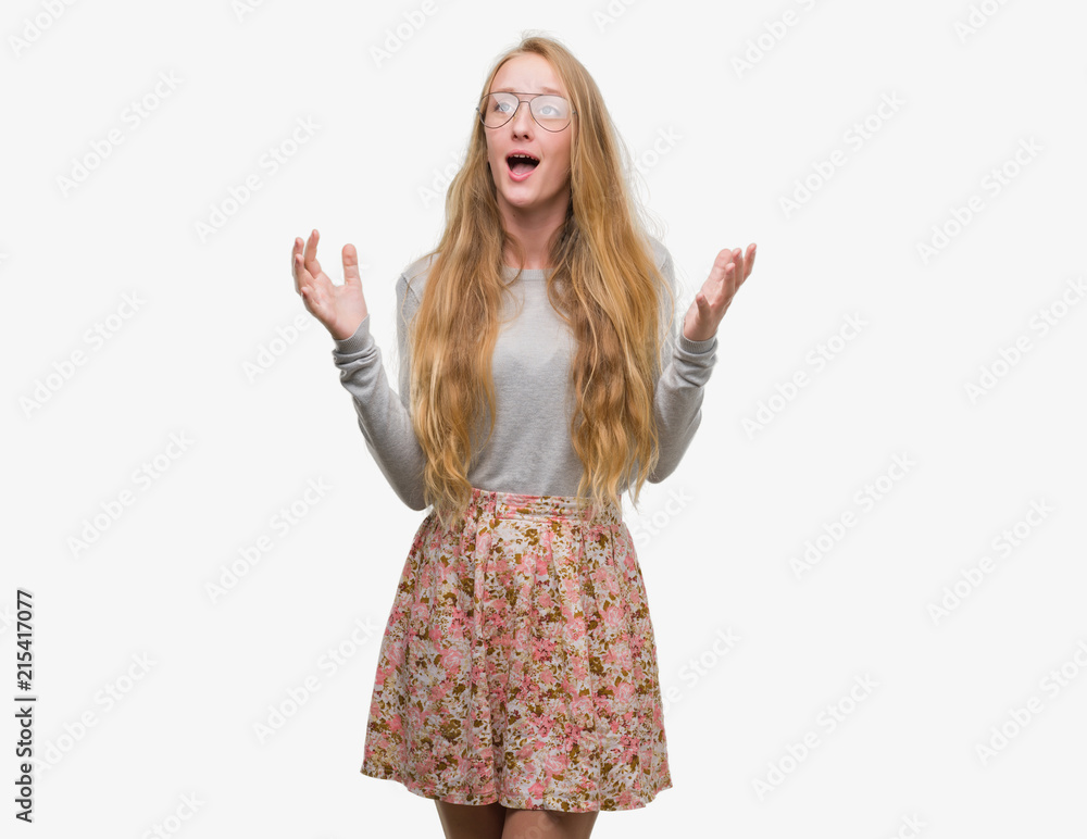 Blonde teenager woman wearing flowers skirt crazy and mad shouting and yelling with aggressive expression and arms raised. Frustration concept. Blonde teenager woman wearing flowers skirt crazy and mad shouting and yelling with aggressive expression and arms raised. Frustration concept.