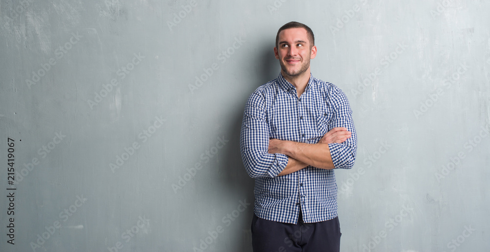 Young caucasian man over grey grunge wall smiling looking side and staring away thinking. Young caucasian man over grey grunge wall smiling looking side and staring away thinking.
