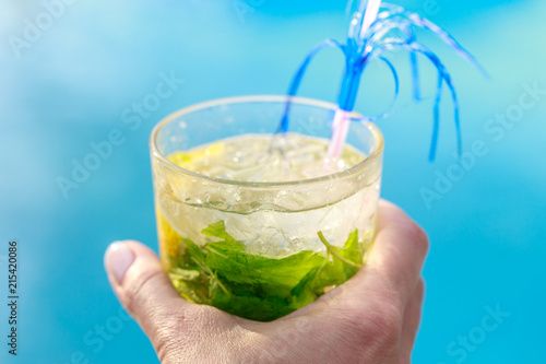 Large glass of cocktail with mint and lemon in hand on a blue background close-up
