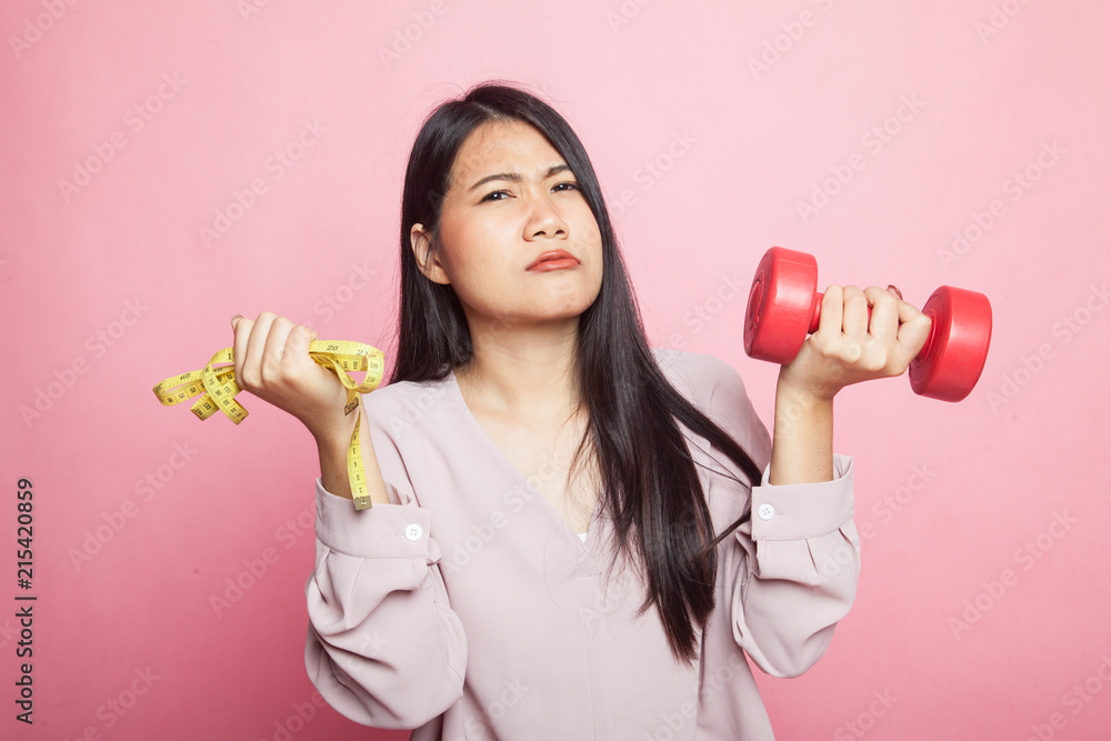 Exhausted Asian woman with dumbbells and measuring tape. Exhausted Asian woman with dumbbells and measuring tape.
