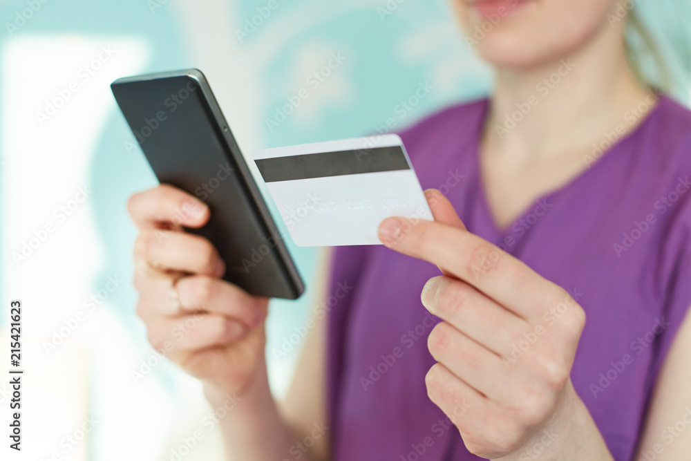 Cropped image of modern smart phone and plastic card in woman`s hands against blue blurred background. Young businesswoman checks her bank account in mobile application. Online payment concept