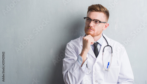 Foto Young redhead doctor man over grey grunge wall serious face thinking about quest