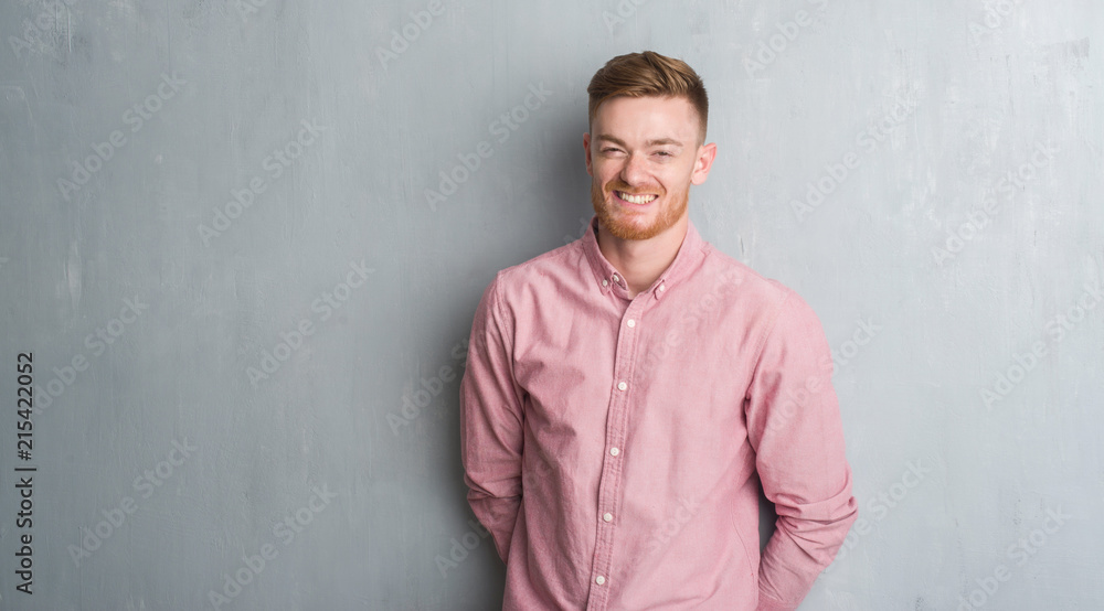 Young redhead man over grey grunge wall wearing pink shirt with a happy and cool smile on face. Lucky person. Young redhead man over grey grunge wall wearing pink shirt with a happy and cool smile on face. Lucky person.