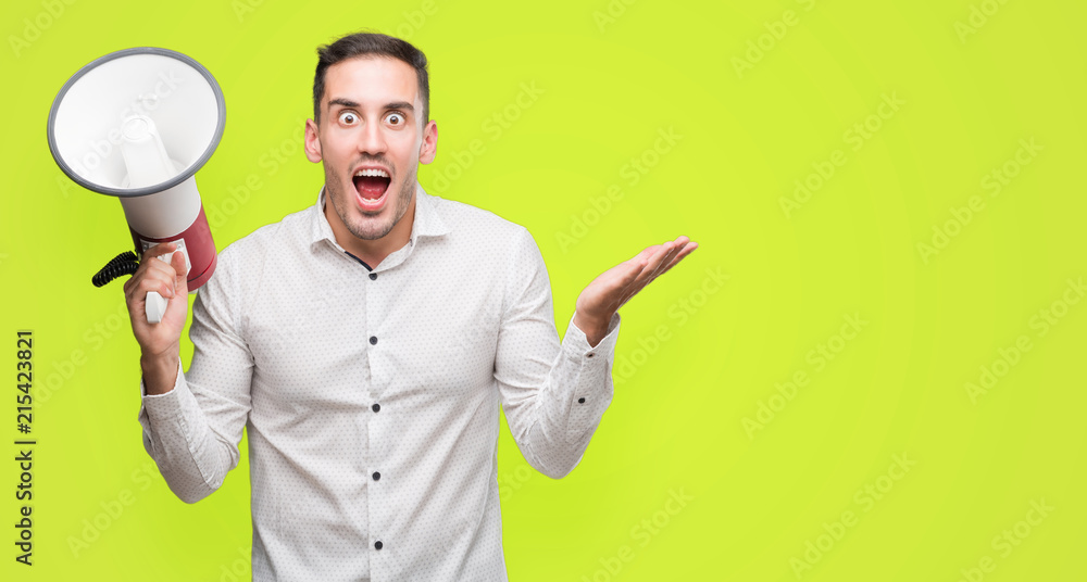 Handsome young man holding microphone very happy and excited, winner expression celebrating victory screaming with big smile and raised hands Handsome young man holding microphone very happy and excited, winner expression celebrating victory screaming with big smile and raised hands