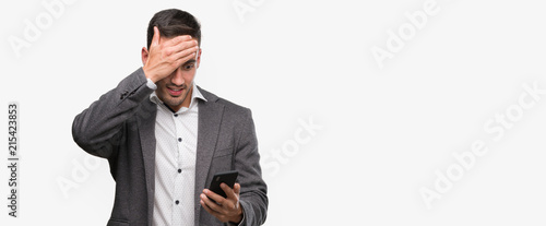 Handsome young man using smartphone stressed with hand on head, shocked with shame and surprise face, angry and frustrated. Fear and upset for mistake.