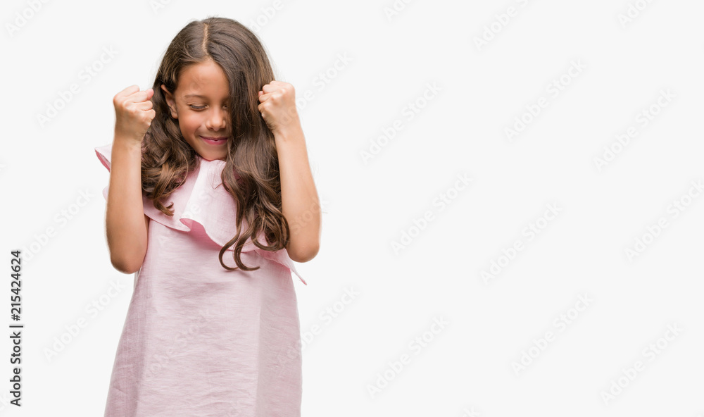 Brunette hispanic girl wearing pink dress excited for success with arms raised celebrating victory smiling. Winner concept. Brunette hispanic girl wearing pink dress excited for success with arms raised celebrating victory smiling. Winner concept.
