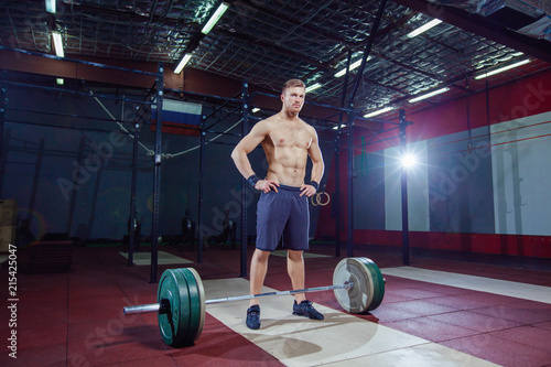 portrait of a muscular man workout with barbell at gym. stands near the bar  resting.