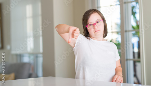 Down syndrome woman at home with angry face, negative sign showing dislike with thumbs down, rejection concept