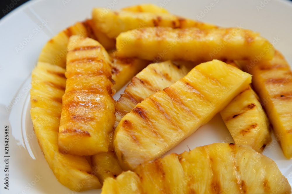 Grilled pineapple wedges on a white plate, closeup. Summer food. Side view. Grilled pineapple wedges on a white plate, closeup. Summer food. Side view.