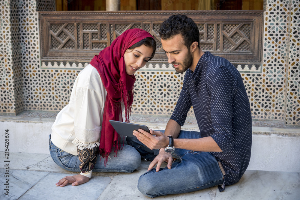 Young Muslim couple in relationship smiling while working on tablet Young Muslim couple in relationship smiling while working on tablet