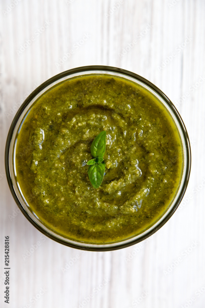 Bowl of freshly made basil pesto on white wooden table, top view. Closeup. Bowl of freshly made basil pesto on white wooden table, top view. Closeup.
