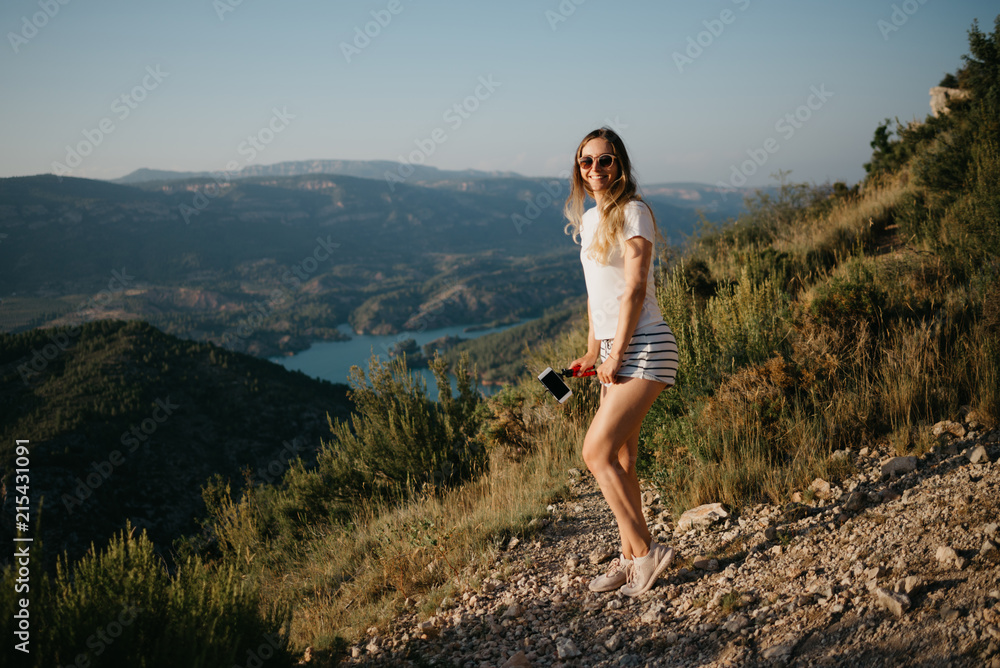 Cute girl dancing on the sandy road with canyon and emerald lake on the background on the sunset in Spain. Traveler in the mountains.