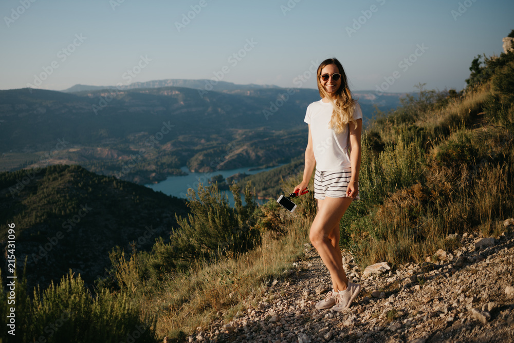 Cute girl enjoying on the sandy road with canyon and emerald lake on the background on the sunset in Spain. Traveler in the mountains.