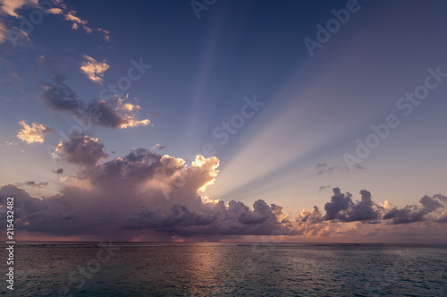 Sun rays behind tropical clouds over ocean at sunset