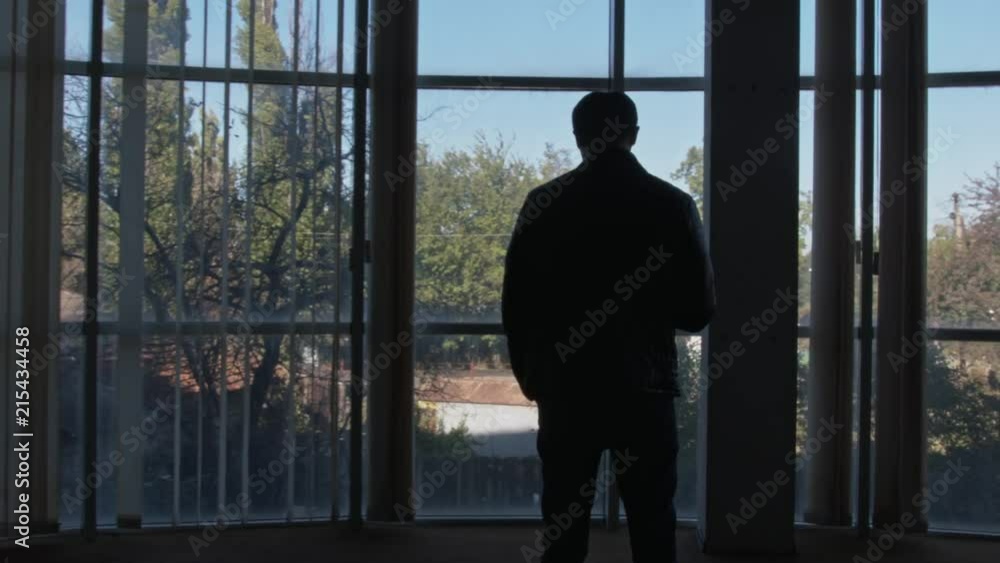 Zoom In From the Back On A Young Man Standing in Front of a Huge Window and Holding His Phone Zoom In From the Back On A Young Man Standing in Front of a Huge Window and Holding His Phone
