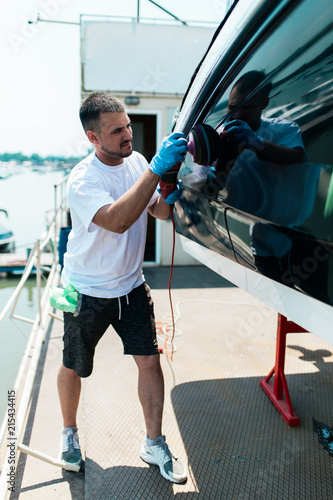 Boat maintenance - Man with orbital polisher polishing boat in marina.