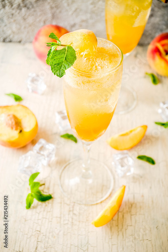 Summer cold alcohol beverage, iced peach Bellini cocktail with mint leaves, light concrete background copy space