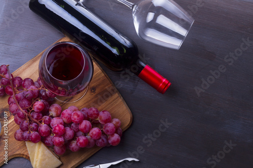 Bottle of red wine and two wine glasses - oned filed and empty one, on table with grape, banner