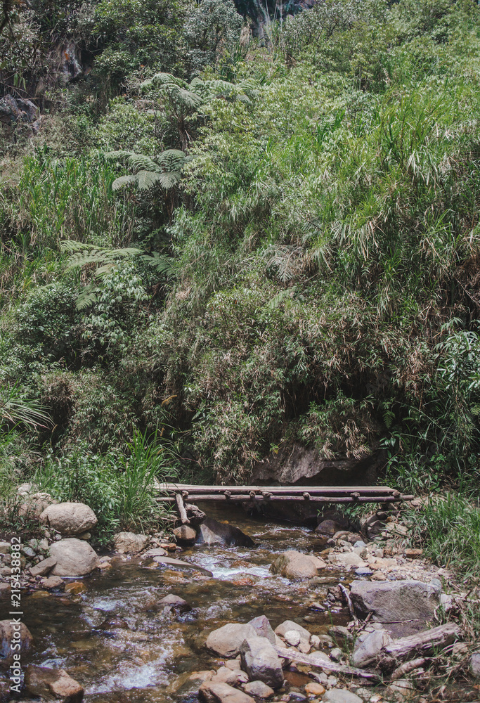 Small wooden bridge over a river leading to a waterfall on the famous Road of Waterfalls in Baños, Ecuador Small wooden bridge over a river leading to a waterfall on the famous Road of Waterfalls in Baños, Ecuador