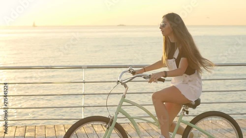 Young attractive woman riding vintage bike near the sea during sunrise or sunset photo