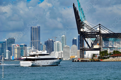 Motor yacht cruising by Port of Miami cargo loading cranes with downtown Miami building skyline in the background © Wimbledon
