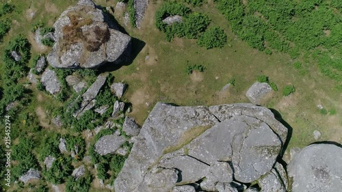 Top down aerial tracking backwards over a rocky outcrop with large boulders surrounded by grassy moorland. Dartmoor, England. photo