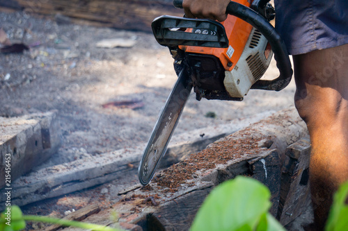 Man uses gasoline engine portable chainsaw cut timber into pieces. Some parts of the man body in the picture.