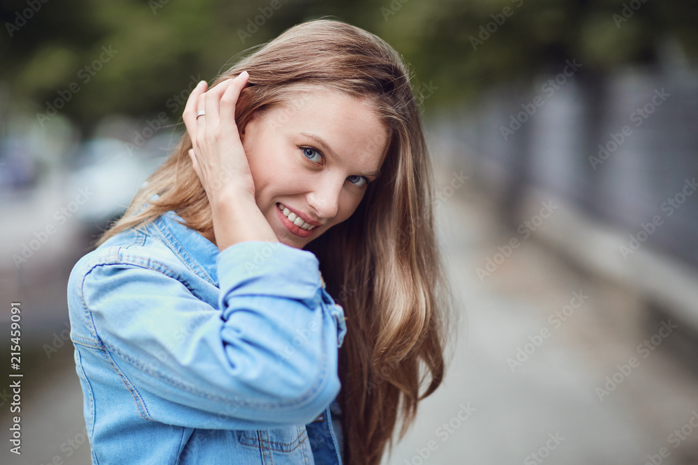 A blonde girl is smiling on a city street. Close-up portrait.