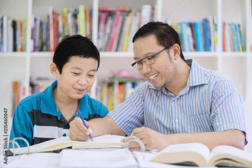 Asian teacher helping his student to read a book Asian teacher helping his student to read a book