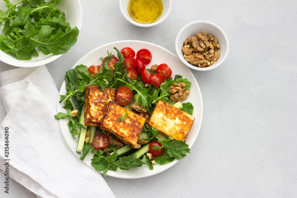 Fresh salad from arugula, cherry tomatoes, cucumbers and roasted cheese on a gray stone background. top view. delicious healthy food. free space Fresh salad from arugula, cherry tomatoes, cucumbers and roasted cheese on a gray stone background. top view. delicious healthy food. free space