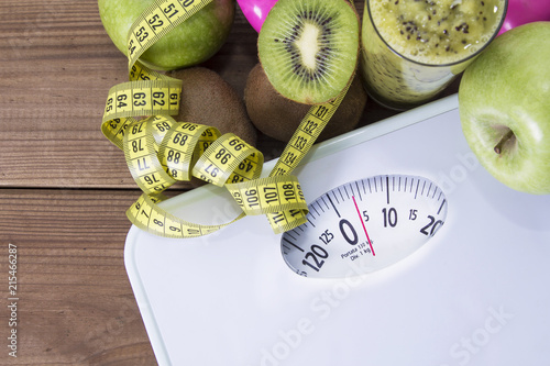scales with measuring tape and green fruits, concept of healthy diet