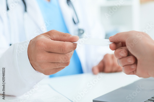 Male doctor s hand give white blank calling card to woman closeup in office. Physical  disease prevention  examine patient  instrument shop  healthy lifestyle  family doctor concept