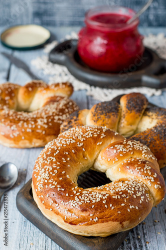 Homemade baking. Fresh ruddy round bagels with sesame and a jar of fruit jam on an old wooden table.