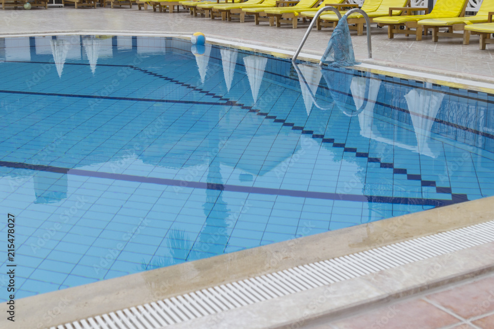 Part of the outdoor swimming pool at the hotel, the ball in the corner of the pool, around the yellow sunbeds.