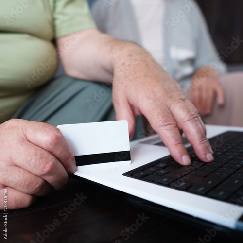 Retirement and technology innovation, people, gadgets, modern lifestyle concept. Retiree couple shopping online using laptop and credit card. Old man hands on keyboard, and senior woman at background