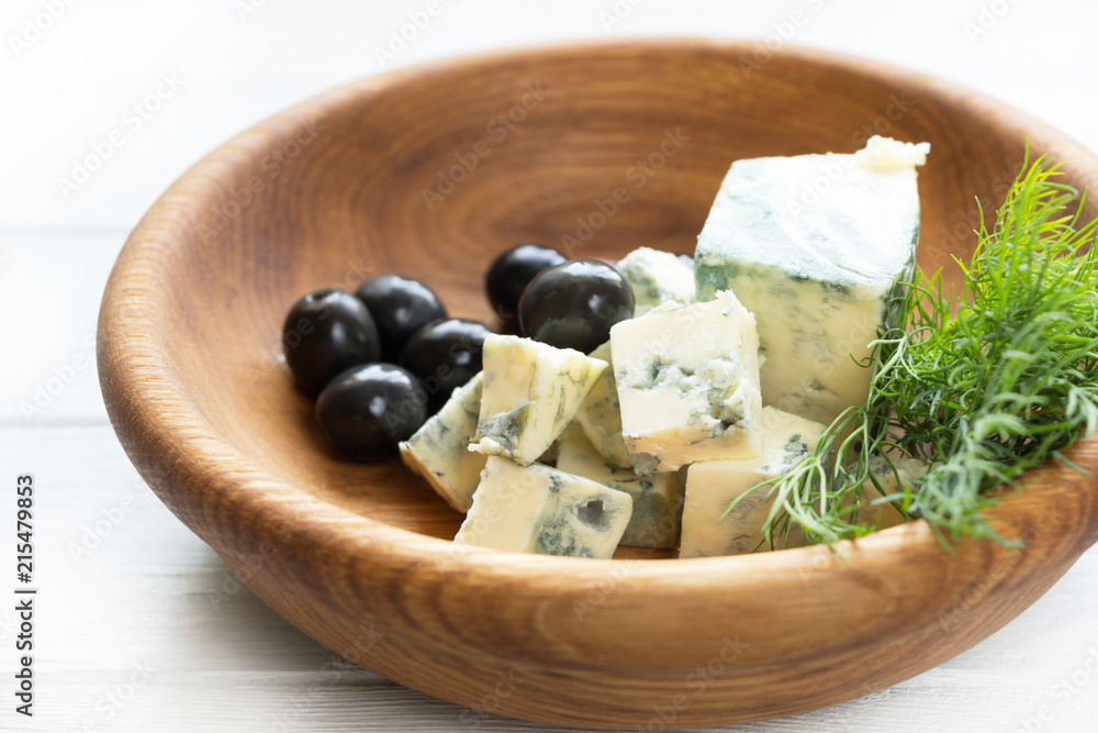 Blue cheese on wooden plate with black olives and herbs. Gourmet food