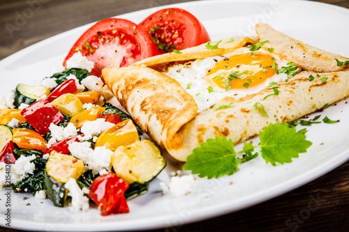 Crepes with eggs on wooden background