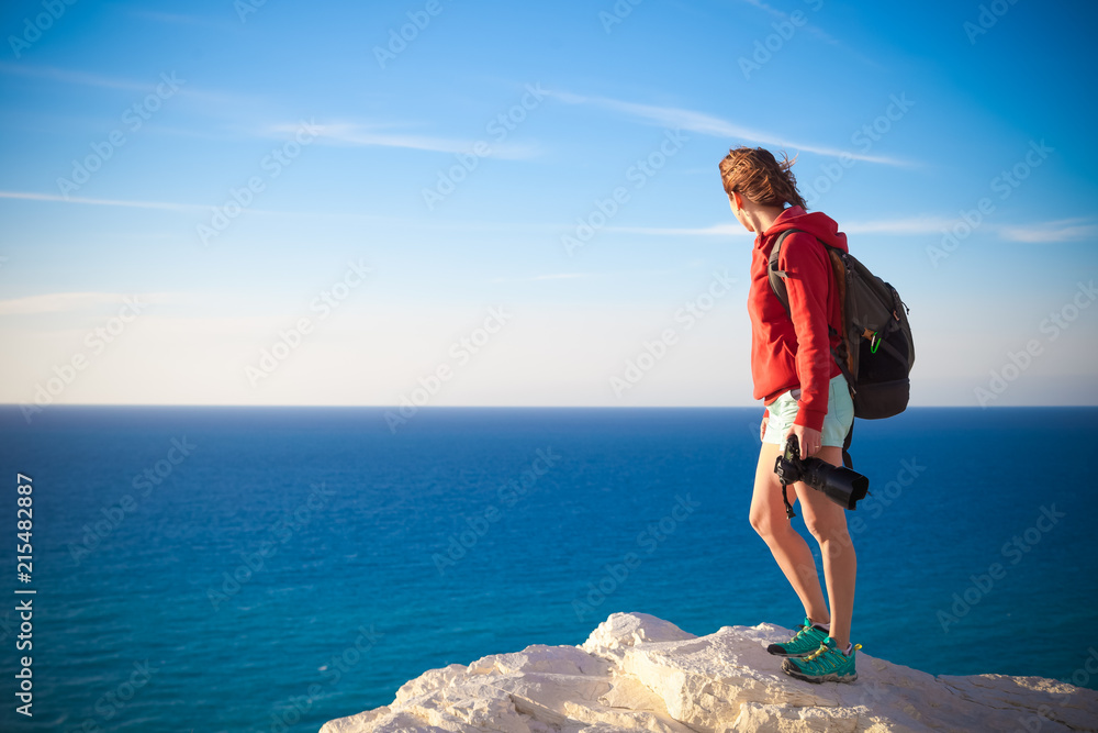 Young professional photographer woman stands with photo camera in hands on rock above the sea, beautiful nature, profession, vacation and travel concept Young professional photographer woman stands with photo camera in hands on rock above the sea, beautiful nature, profession, vacation and travel concept