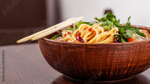 Asian Oriental Cuisine. Japanese noodles with chicken and vegetables, sesame and parsley, in a plate of red clay, stands on a table in a restaurant. Copy space, selective focus